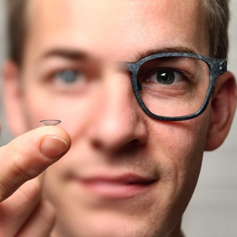 Mann hält eine Kontaktlinse und blickt durch eine Brille mit nur einem Glas.