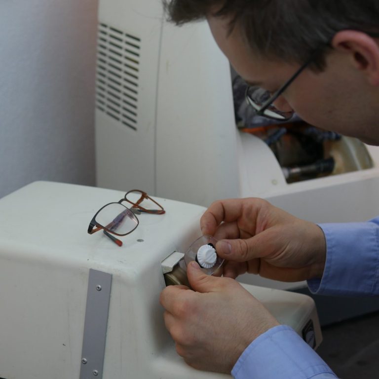 Eine Optiker kantet ein Brillenglas an einem Handschleifautomat ab.