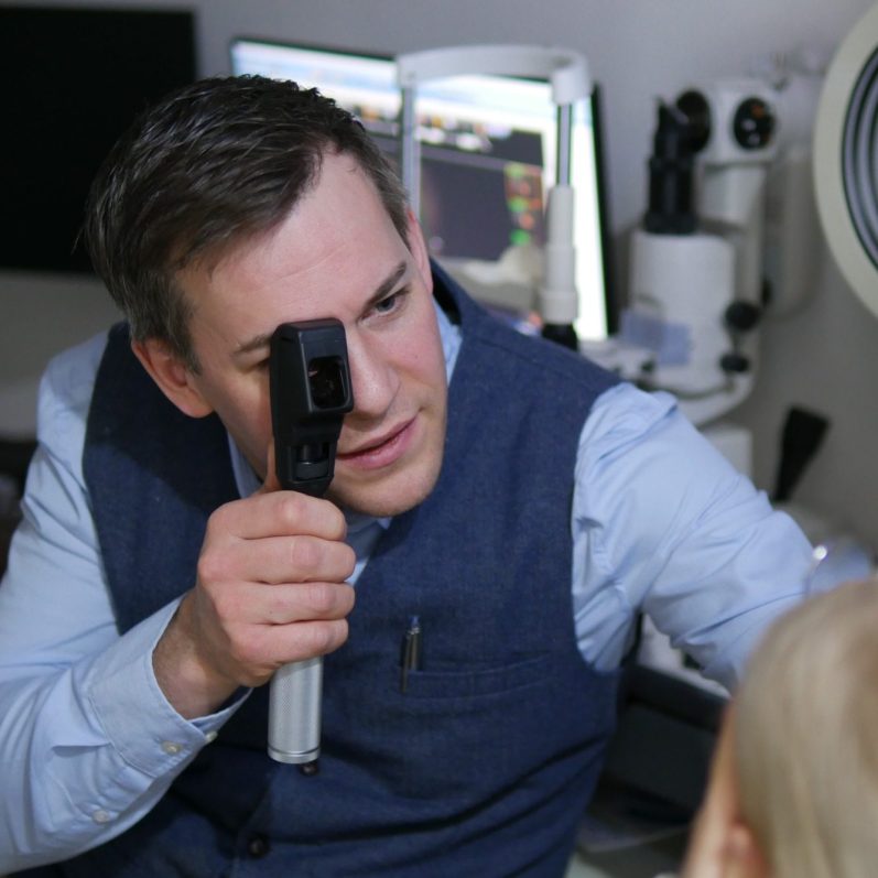 Optiker untersucht das Auge einer Patientin mit einem Skiaskop.