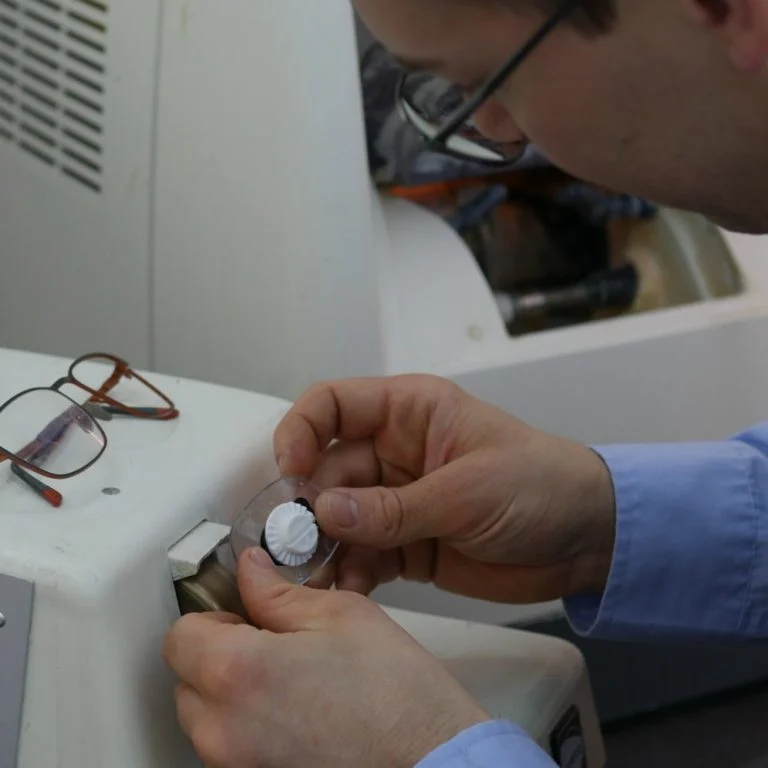 Eine Optiker kantet ein Brillenglas an einem Handschleifautomat ab.